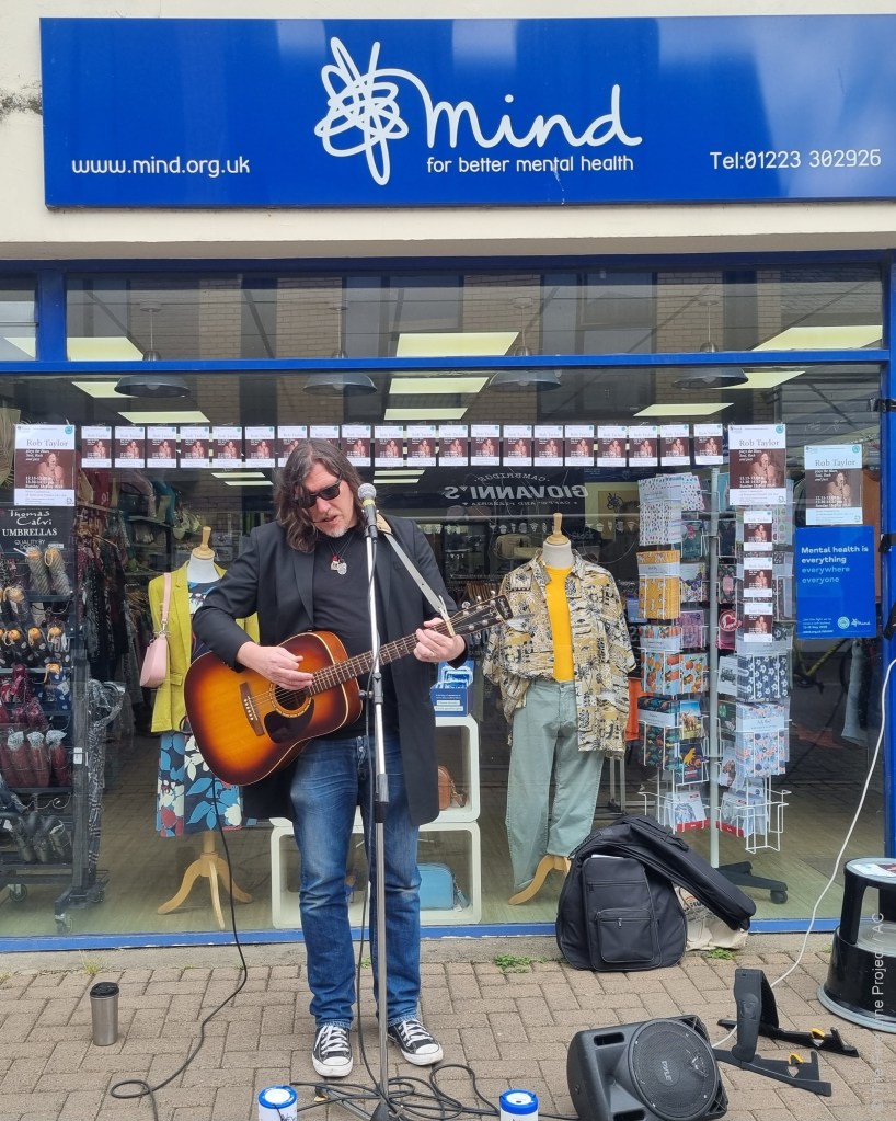 Guitarist Rob Taylor performing outside the Mind Cambridge shop during Mental Health Awareness Week 2025 © The Fine Line Project